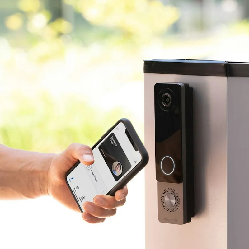 A person using a smartphone credential at an installed Avigilon access-control reader and video intercom